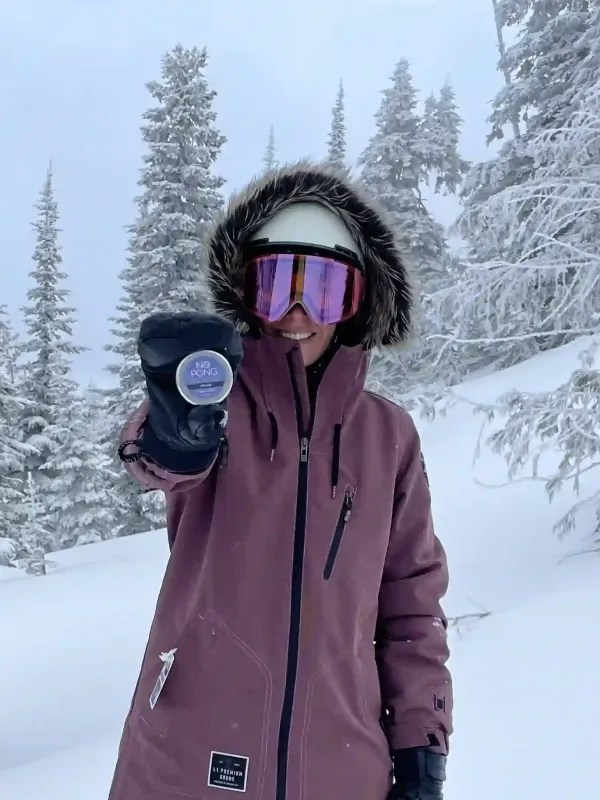 A No Pong customer in a ski jacket and goggles holding up her tin in the snow
