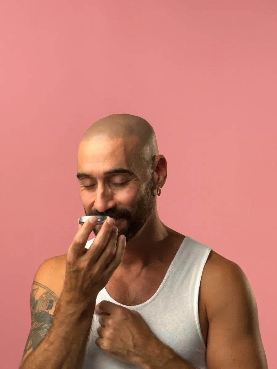 A No Pong customer on a pink background, eyes closed, smelling his open tin